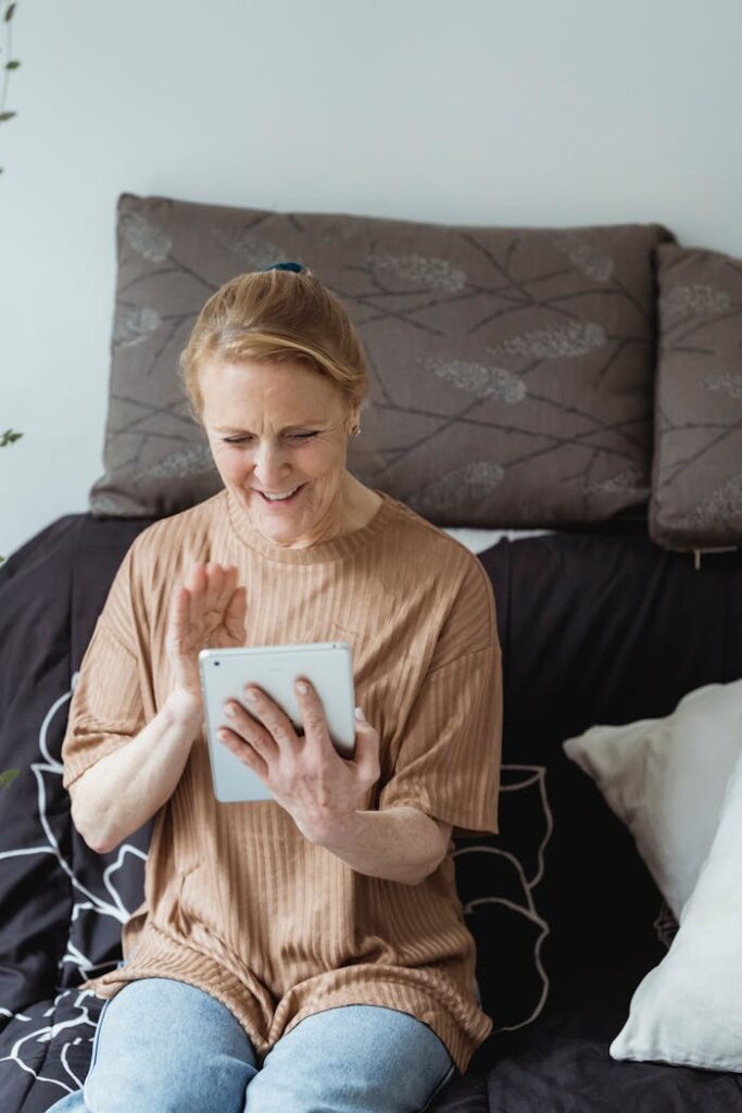 Happy senior woman using a tablet for a video call indoors, smiling and waving.