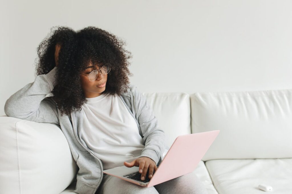 pexels photo 7382391 A woman with curly hair and glasses works remotely on a laptop from her cozy home.